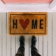 a welcome mat on the ground in front of a pink door that says Home with the O being a red heart