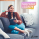 a woman is sitting on a couch with a tablet and the words upgraded comfort above her