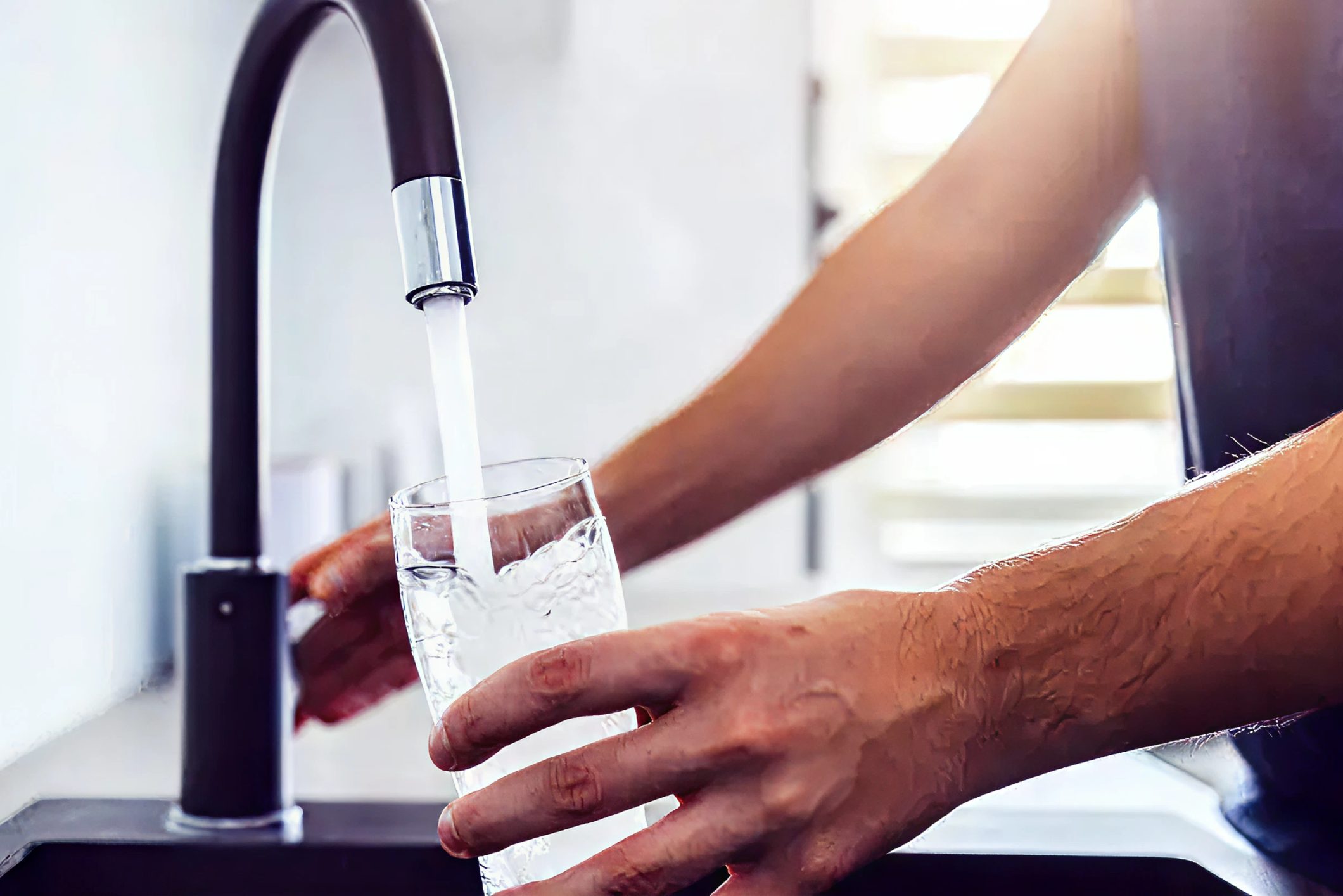 Clean drinking water pouring from a modern matte black faucet into a clear glass.